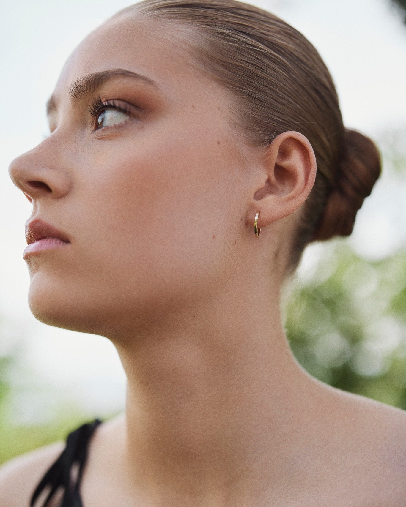 Model wearing a single Medium Hoop earring in recycled 14K gold with a click-closure design.
