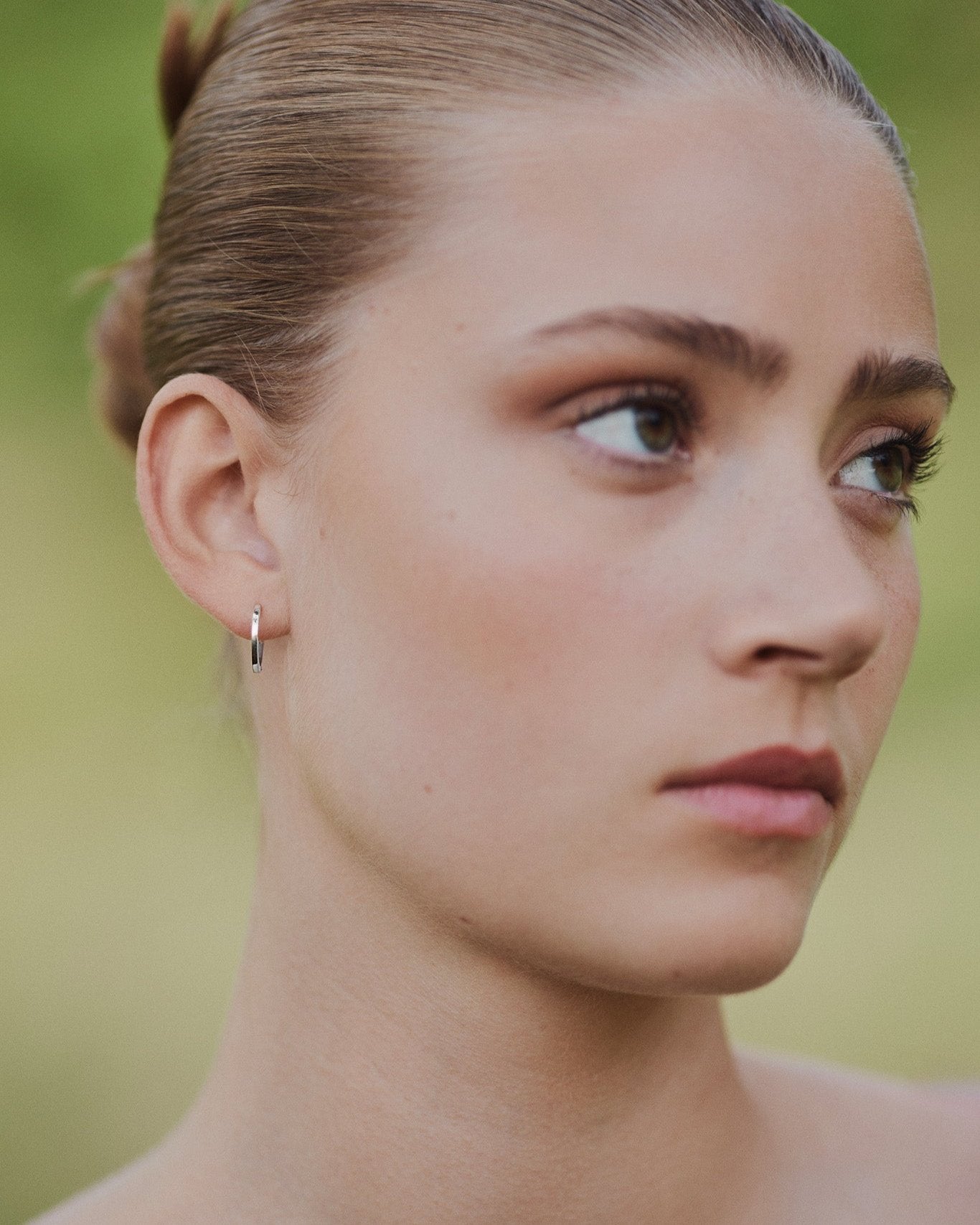 Model wearing a single Medium Hoop earring in recycled 14K white gold with a click-closure design.
