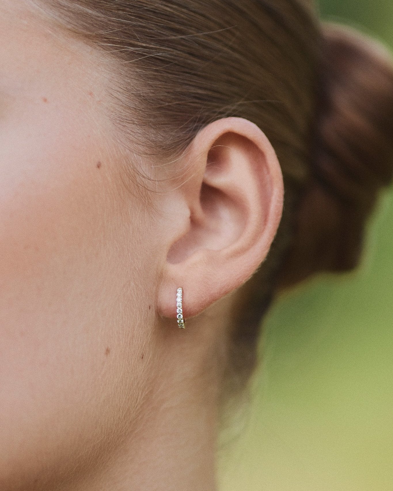 Close-up of an ear wearing a single Small Diamond Hoop earring in recycled 14K white gold, set with 9 lab-grown diamonds in a click-closure design.