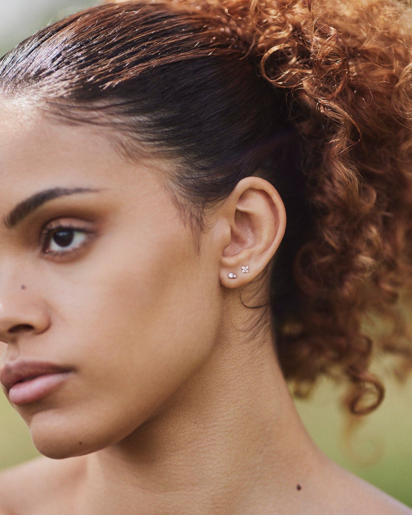 A single gold Flor stud earring shaped like a four-petal flower with a small diamond in the center, shown stacked with our Diamond Duo Stud.